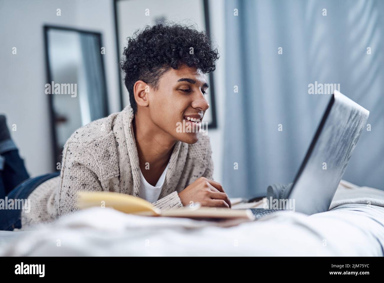 Il letto è la nuova scrivania, un giovane che usa un computer portatile sul letto di casa. Foto Stock