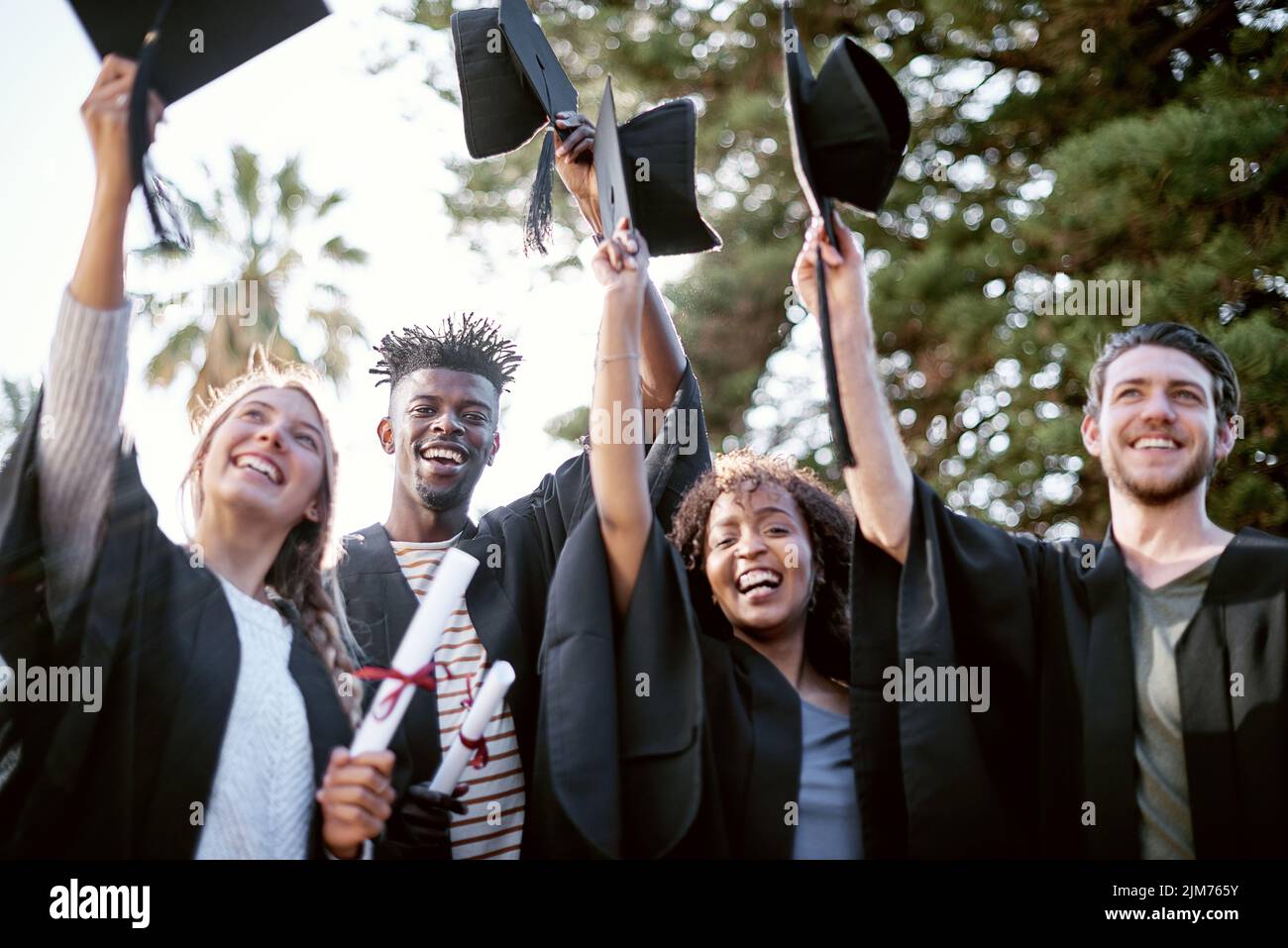 L'istruzione è la chiave per sbloccare la porta d'oro della libertà. Ritratto di un gruppo di studenti che tengono cappelli di sollevamento in festa il giorno della laurea. Foto Stock