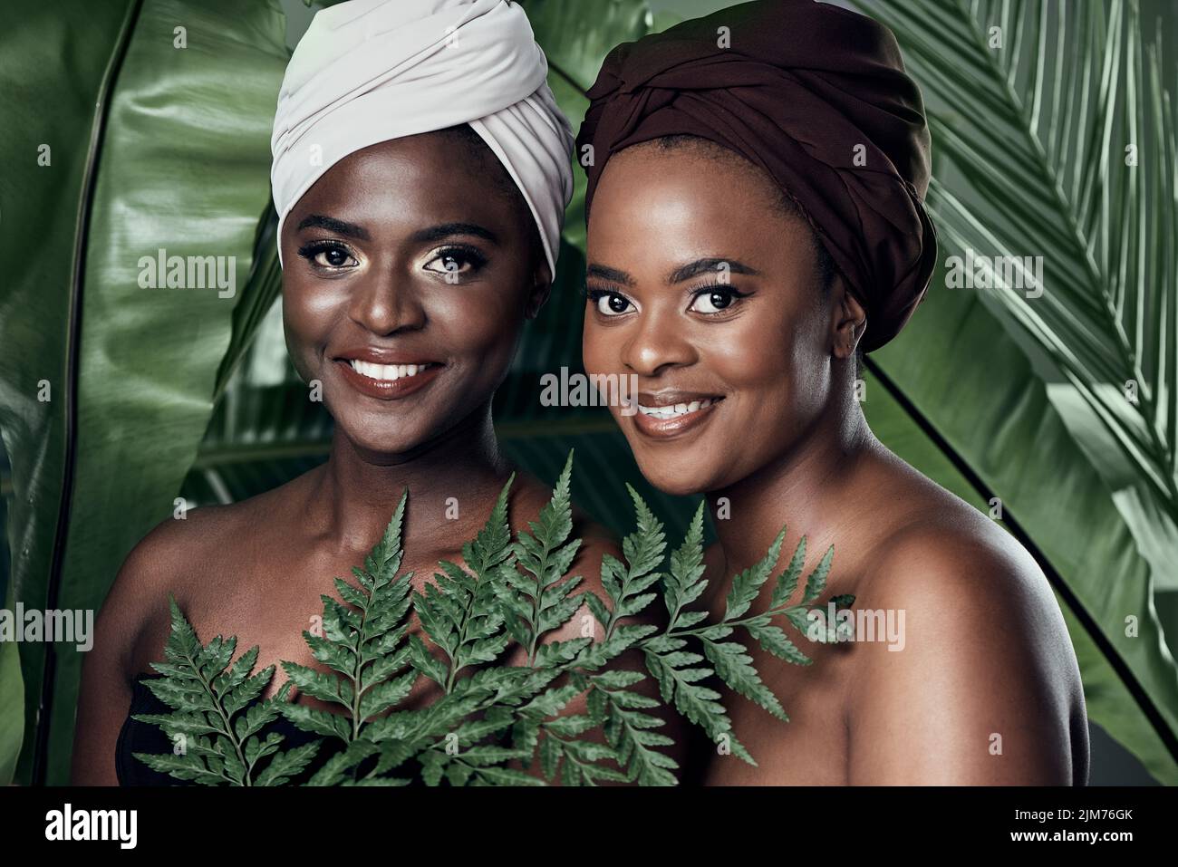 Insieme è un buon posto per essere. Studio ritratto di due belle giovani donne in posa di fronte a foglie di palma su uno sfondo grigio. Foto Stock