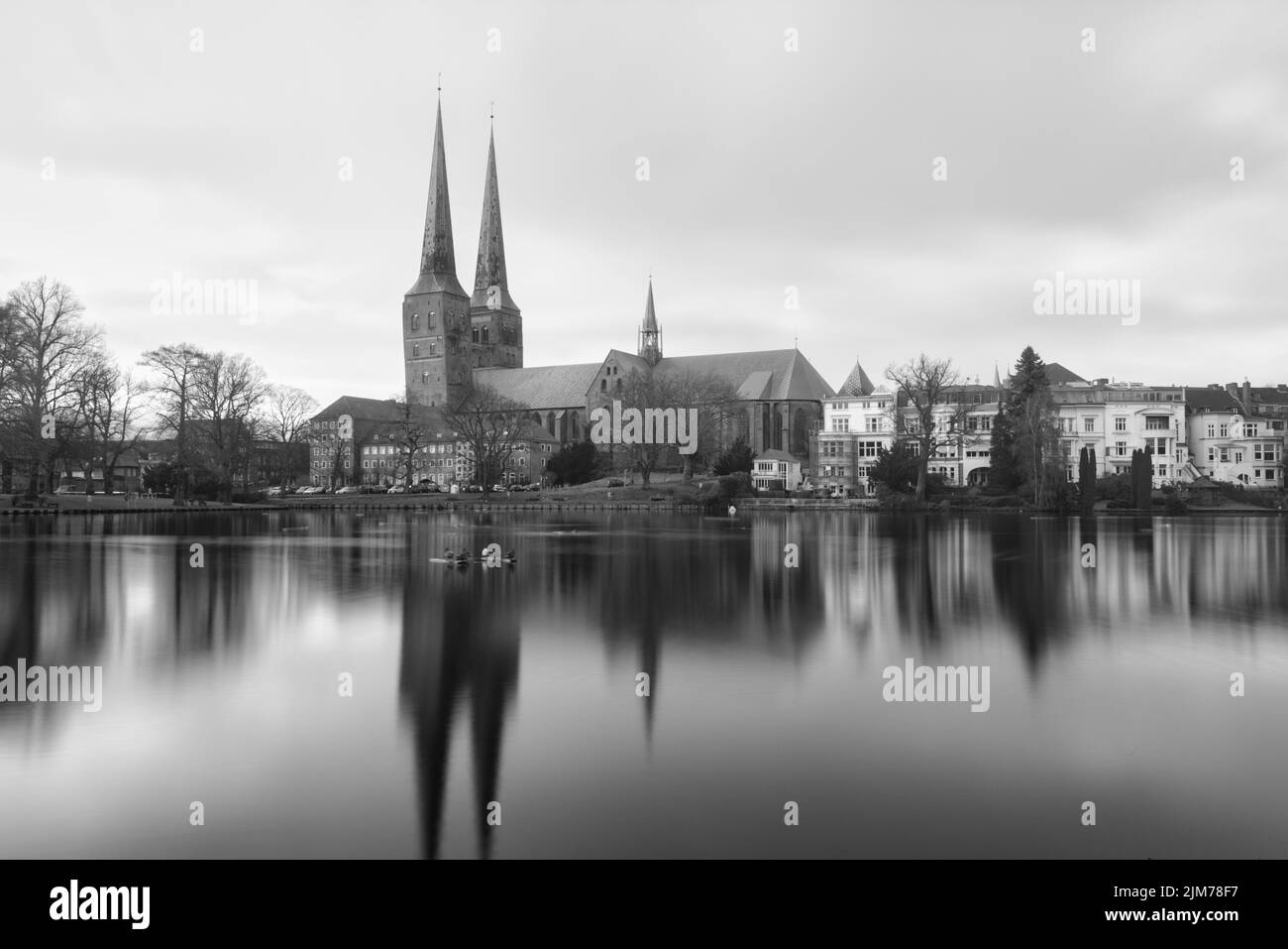 Un'immagine in scala di grigi del paesaggio urbano di Lubecca con la chiesa di Santa Maria riflessa sul fiume trave Foto Stock