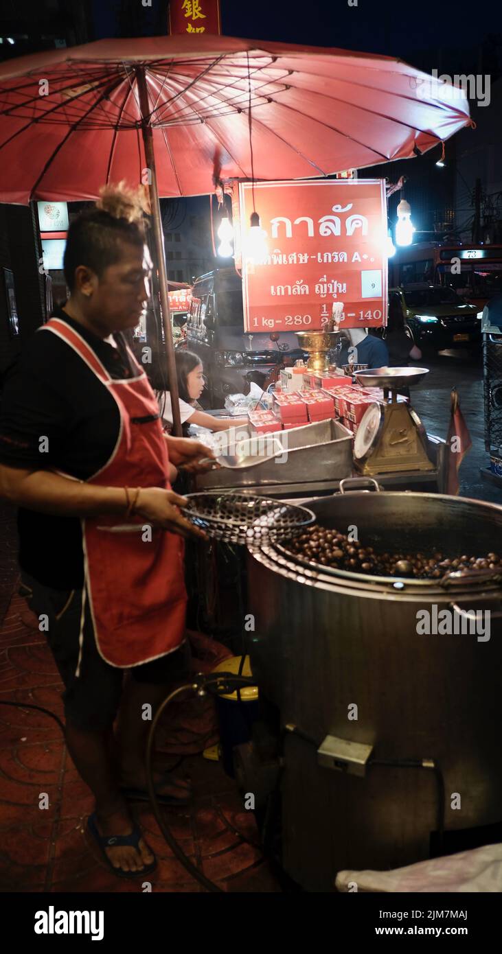 Man Roasting Hot Chestnuts di notte a Chinatown Bangkok Thailandia sotto un ombrello rosso Foto Stock