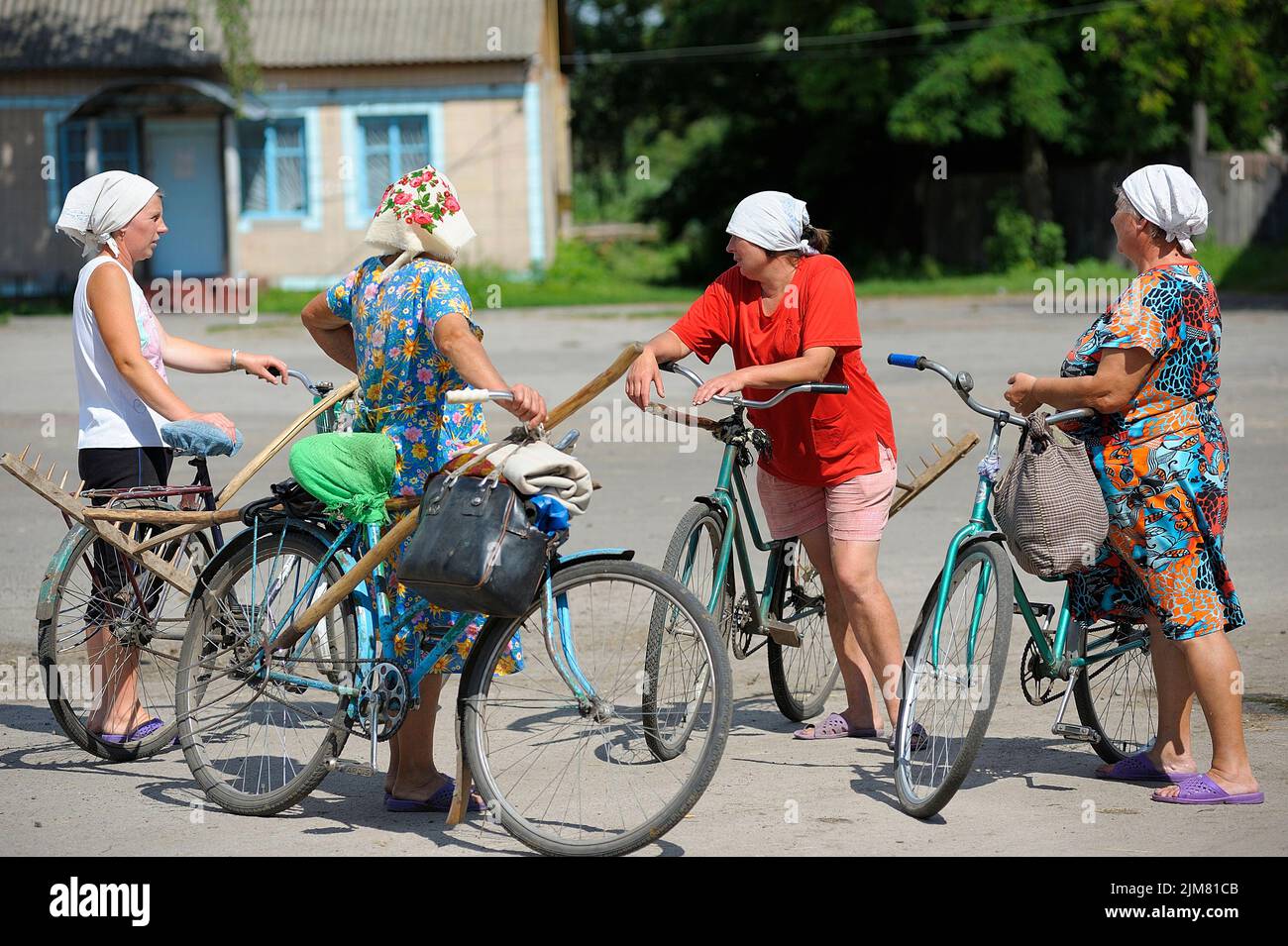 Gruppo di donne casalinghe in piedi con biciclette e borse su una piazza centrale di un villaggio di fronte ad un negozio rurale. Agosto 30, 2019. Mena, Ucraina Foto Stock