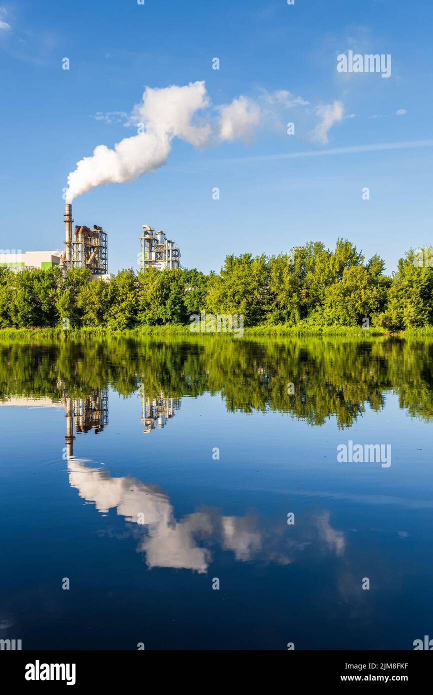 pipe di impresa di lavorazione del legno pianta segheria con bella riflessione in acqua blu del fiume. Concetto di inquinamento atmosferico. Ambienti industriali del paesaggio Foto Stock