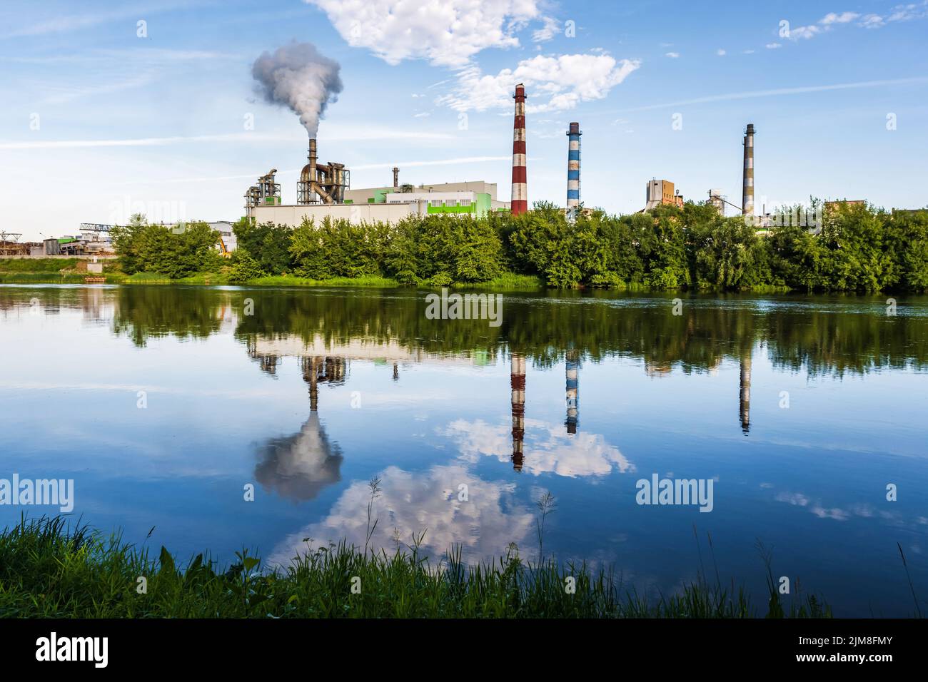 pipe di impresa di lavorazione del legno pianta segheria con bella riflessione in acqua blu del fiume. Concetto di inquinamento atmosferico. Ambienti industriali del paesaggio Foto Stock