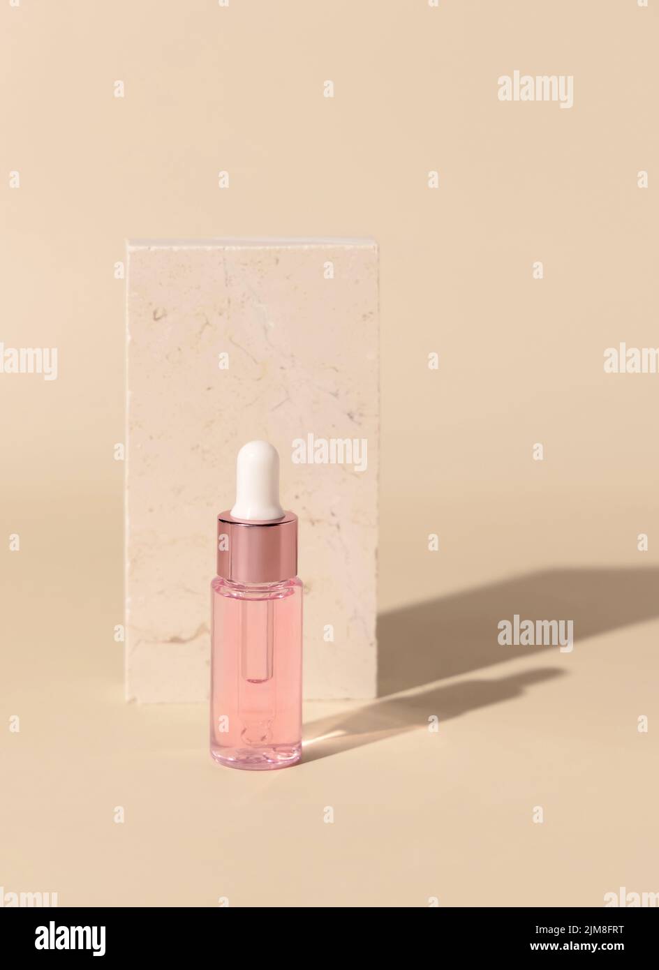 Flacone in vetro cosmetico contagocce vicino alla pietra di travertino su giallo chiaro, primo piano, mockup. Esotico prodotto di bellezza per la cura della pelle, olio essenziale o siero. Pastello Foto Stock