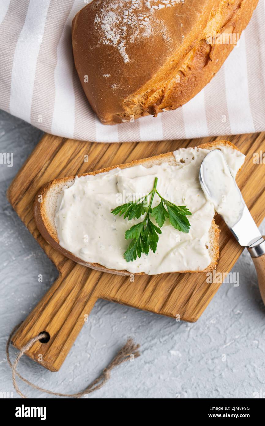 Formaggio cremoso con erbe aromatiche e condimento su fetta di pane fresco di segale croccante con coltello per formaggio nelle vicinanze Foto Stock