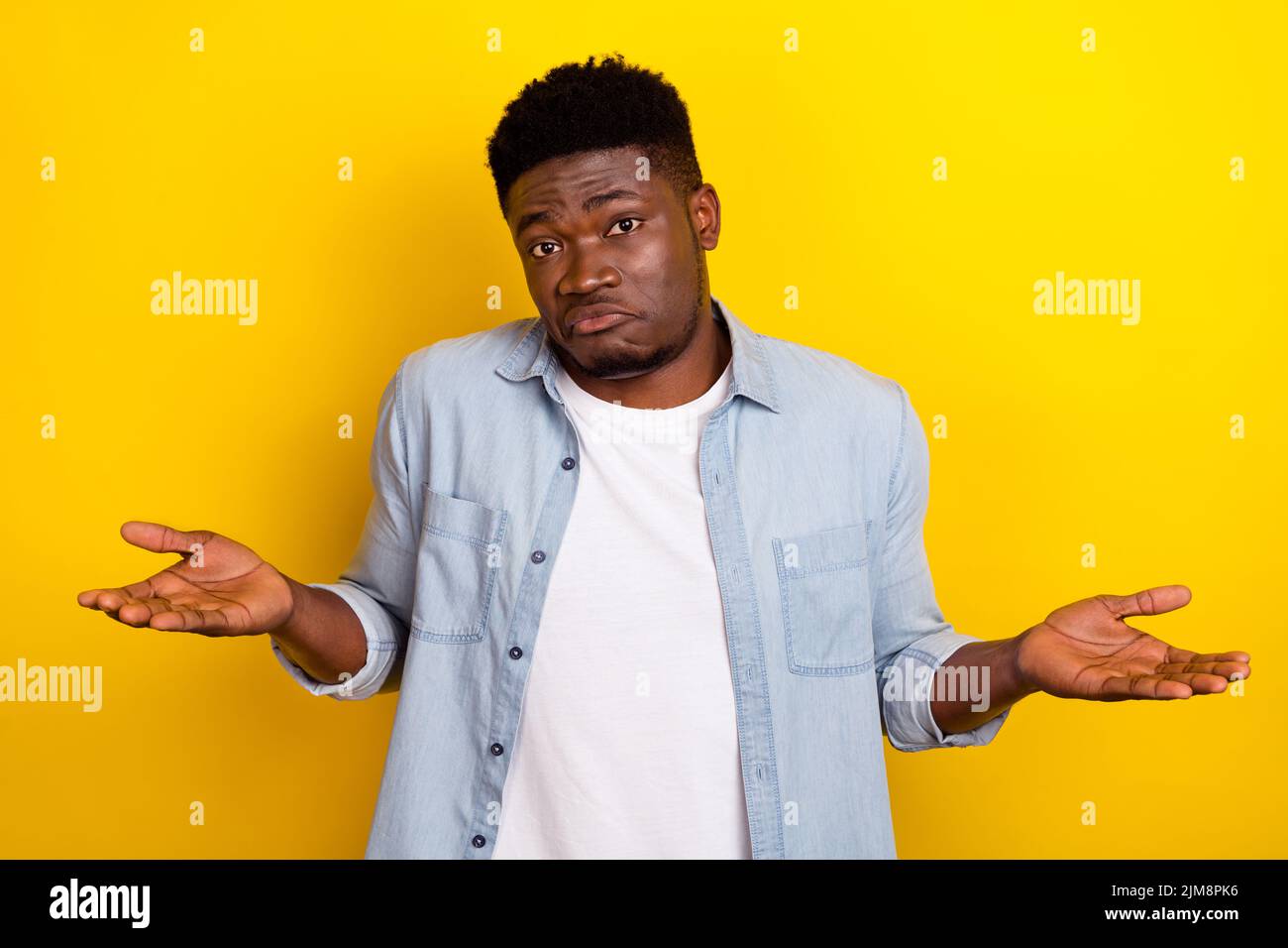 Foto di sconosciuto millennial brunet guy shrug spalle indossare jeans camicia isolato su sfondo giallo Foto Stock