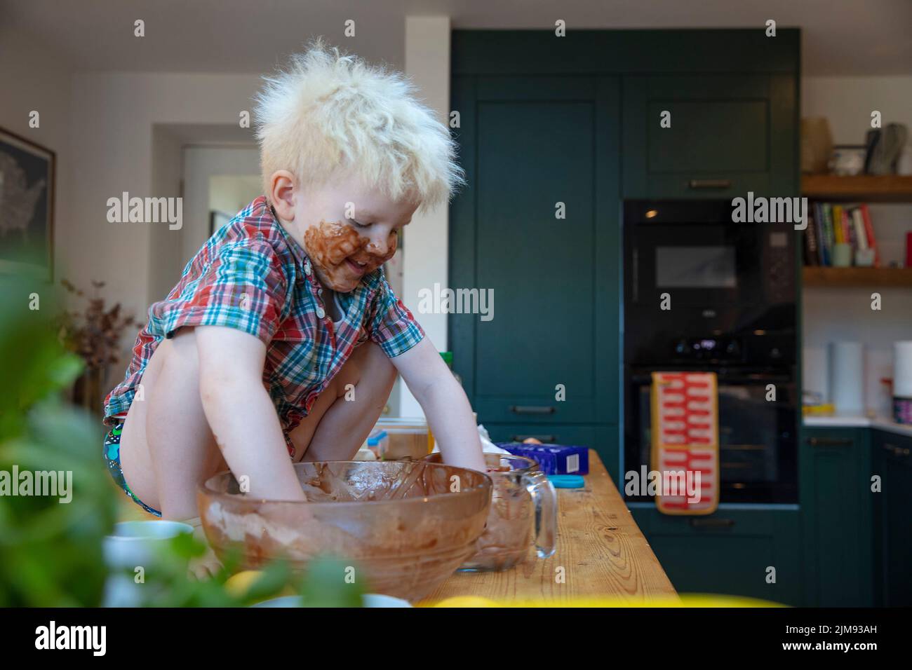 Un ragazzino con mani e viso ricoperti di cioccolato dopo aver aiutato in cucina a cuocere una torta Foto Stock