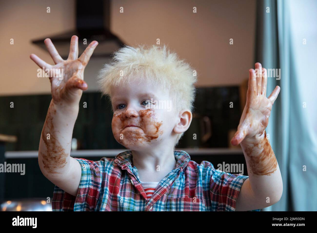 Un ragazzino con mani e viso ricoperti di cioccolato dopo aver aiutato in cucina a cuocere una torta Foto Stock