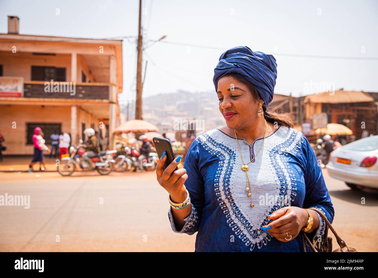 Una donna africana usa il suo smartphone mentre si trova nel centro della città, indossa abiti tradizionali africani Foto Stock
