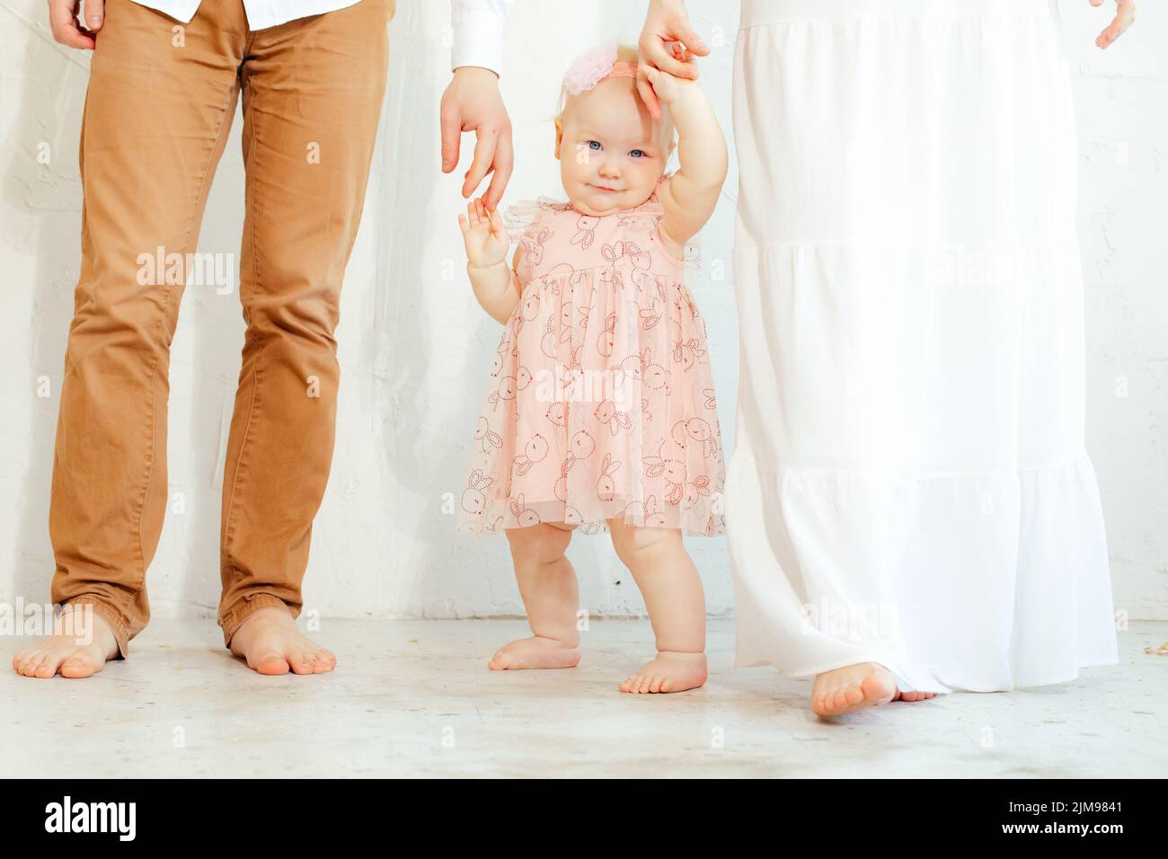 Foto di studio ritagliata di felice, timida, sorridente bambina a piedi nudi in abito rosa e bandelet che tiene le braccia insieme Foto Stock