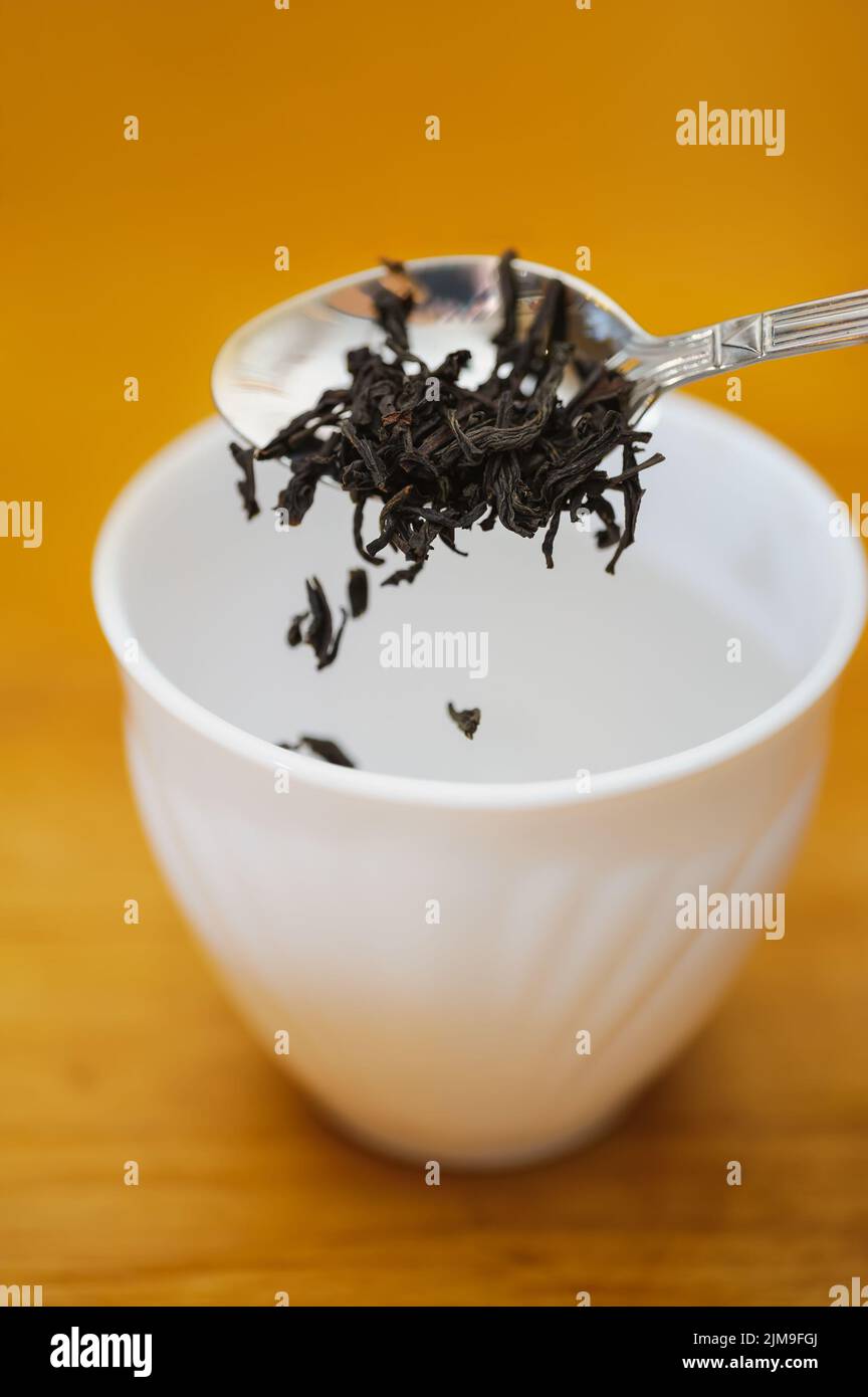 Far cadere il tè nero secco nella tazza Foto Stock