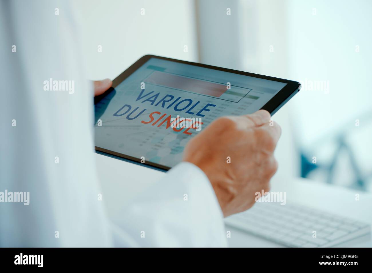 un dottore, indossando un cappotto bianco, tiene in mano un tablet digitale che legge il testo di scimmietta scritto in francese Foto Stock