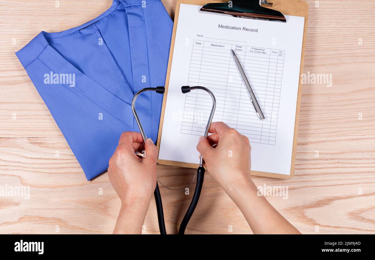 Dottore che raccoglie stetoscopio con oggetti medici di base su scrivania di legno Foto Stock