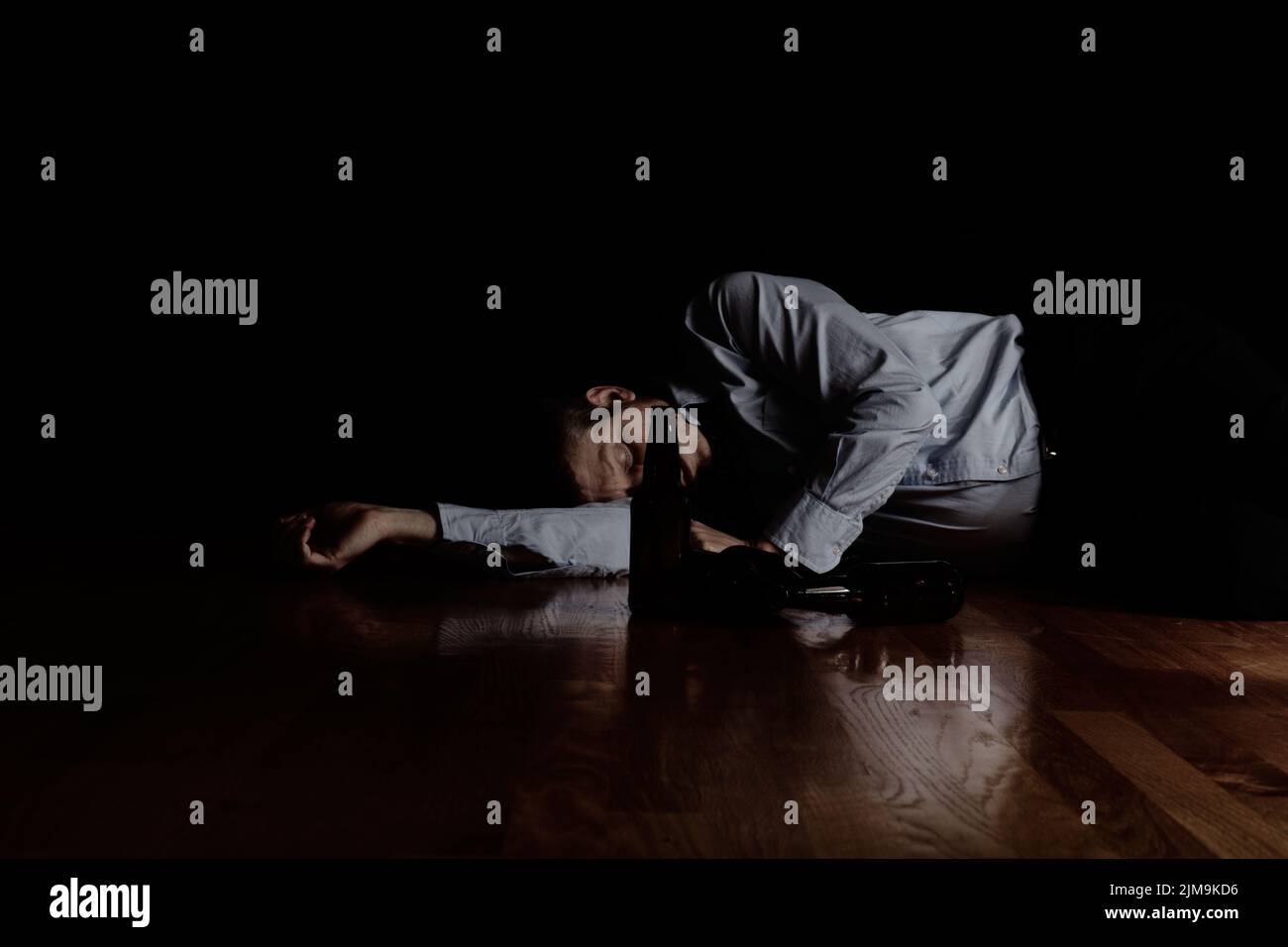 Uomo maturo che dorme sul pavimento dopo aver bevuto troppo con sfondo scuro Foto Stock