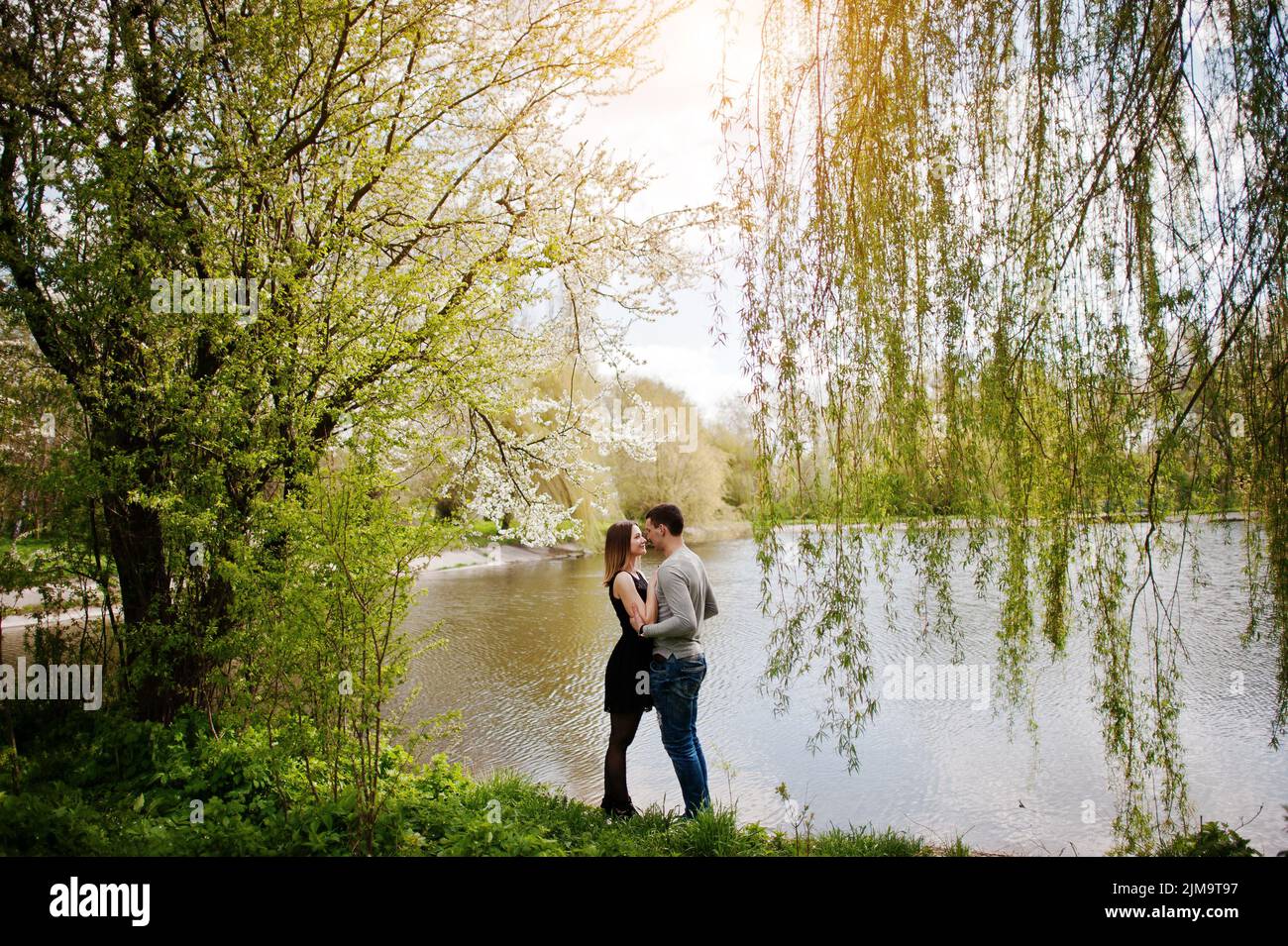 Coppia giovane in amore soggiorno all'aperto vicino al lago con gli alberi di salice Foto Stock