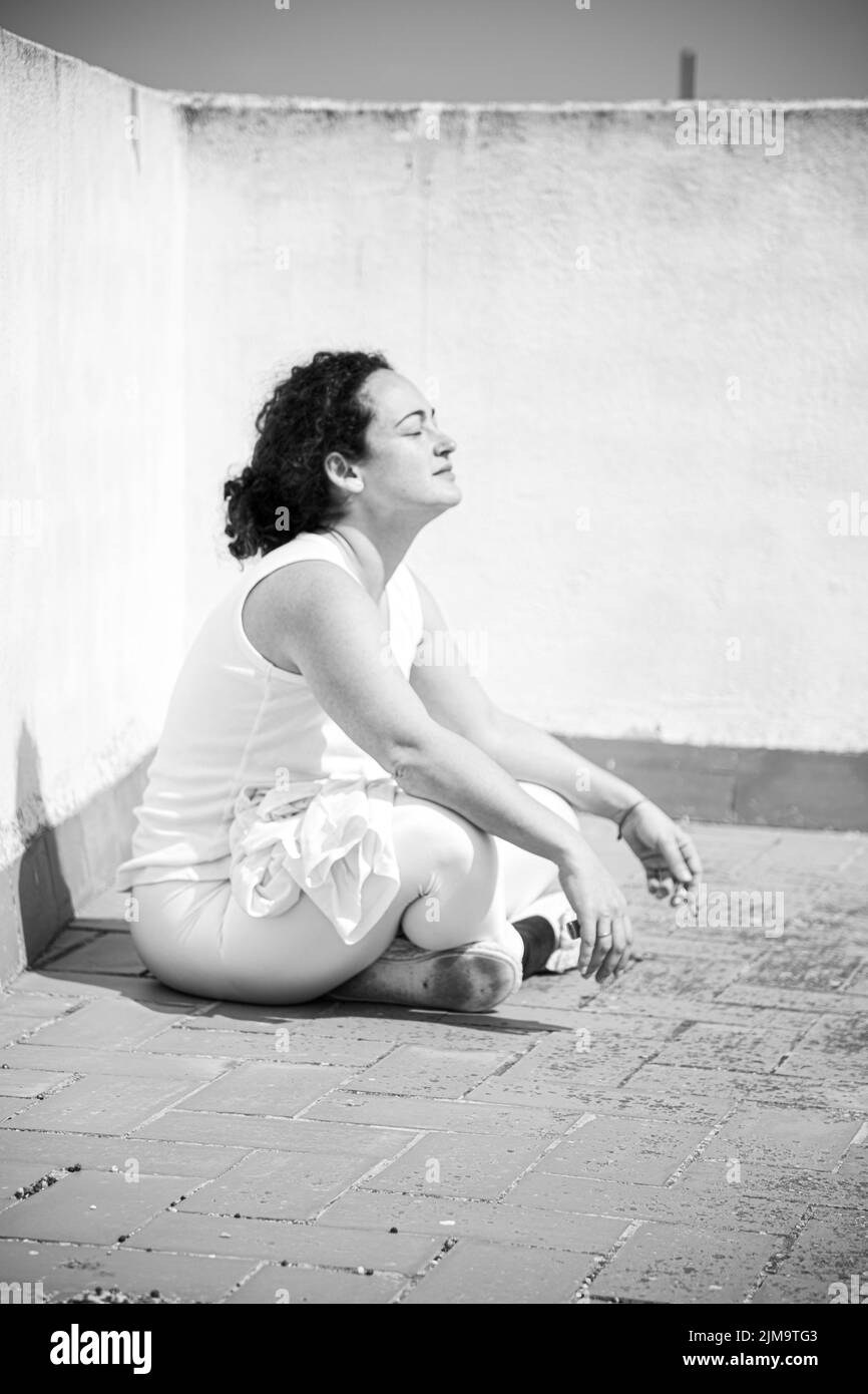 Una foto in bianco e nero di una giovane donna in tuta bianca che prende sole sulla terrazza. Foto Stock