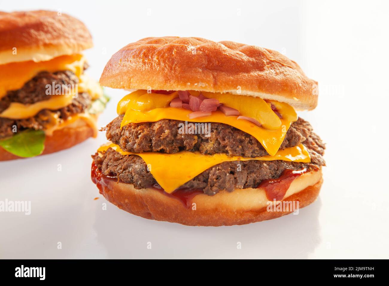 Brioche donut doppio hamburger di manzo al piano con salsa queso con un altro hamburger sullo sfondo. Foto Stock