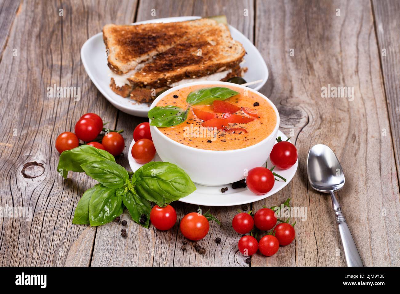 Ciotola fresca di cremosa zuppa di pomodoro e sandwich con foglie di basilico su rustiche tavole di legno Foto Stock