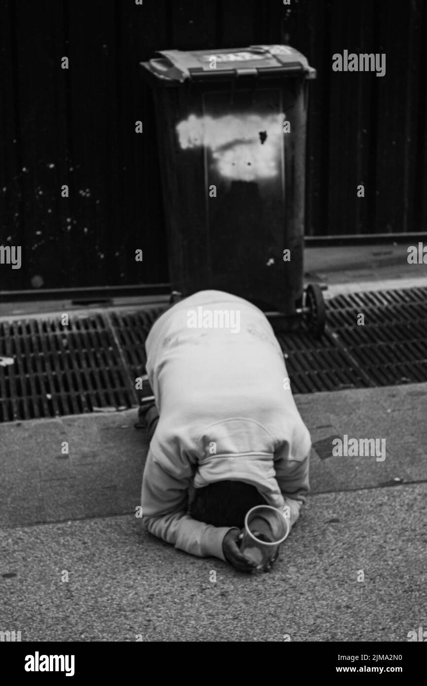 Una povera persona che chiede elemosina per le strade di Madrid in posizione di ginocchia in scala di grigi Foto Stock