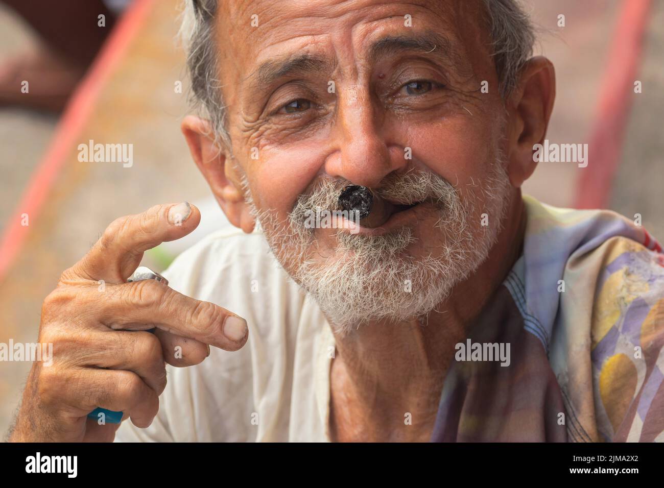 Un primo piano di un vecchio felice con il tabacco in bocca guardando una macchina fotografica Foto Stock