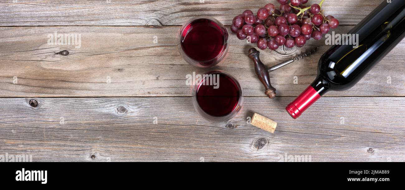 Bottiglia di vino rosso non aperta e bicchieri con uva su tavole rustiche di legno Foto Stock