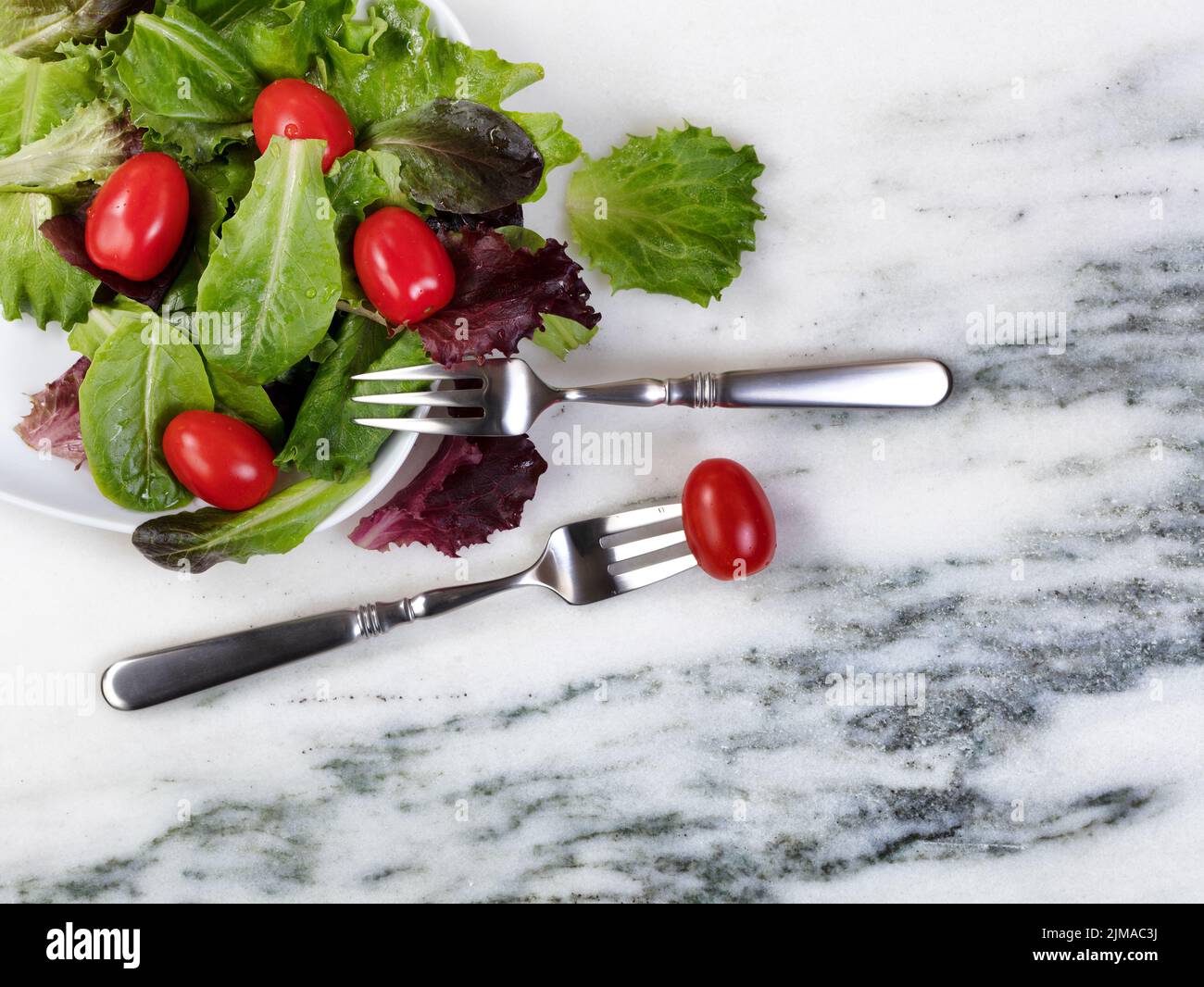 Insalata biologica sana che esce dal piatto su fondo tavola in marmo naturale Foto Stock