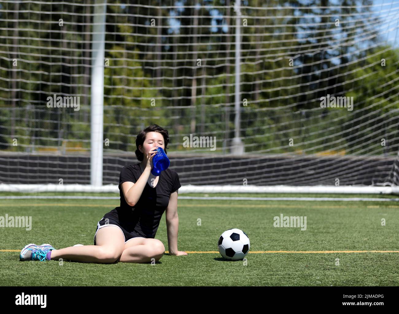 Ragazza teen che beve molta acqua durante una giornata calda sul campo da calcio Foto Stock