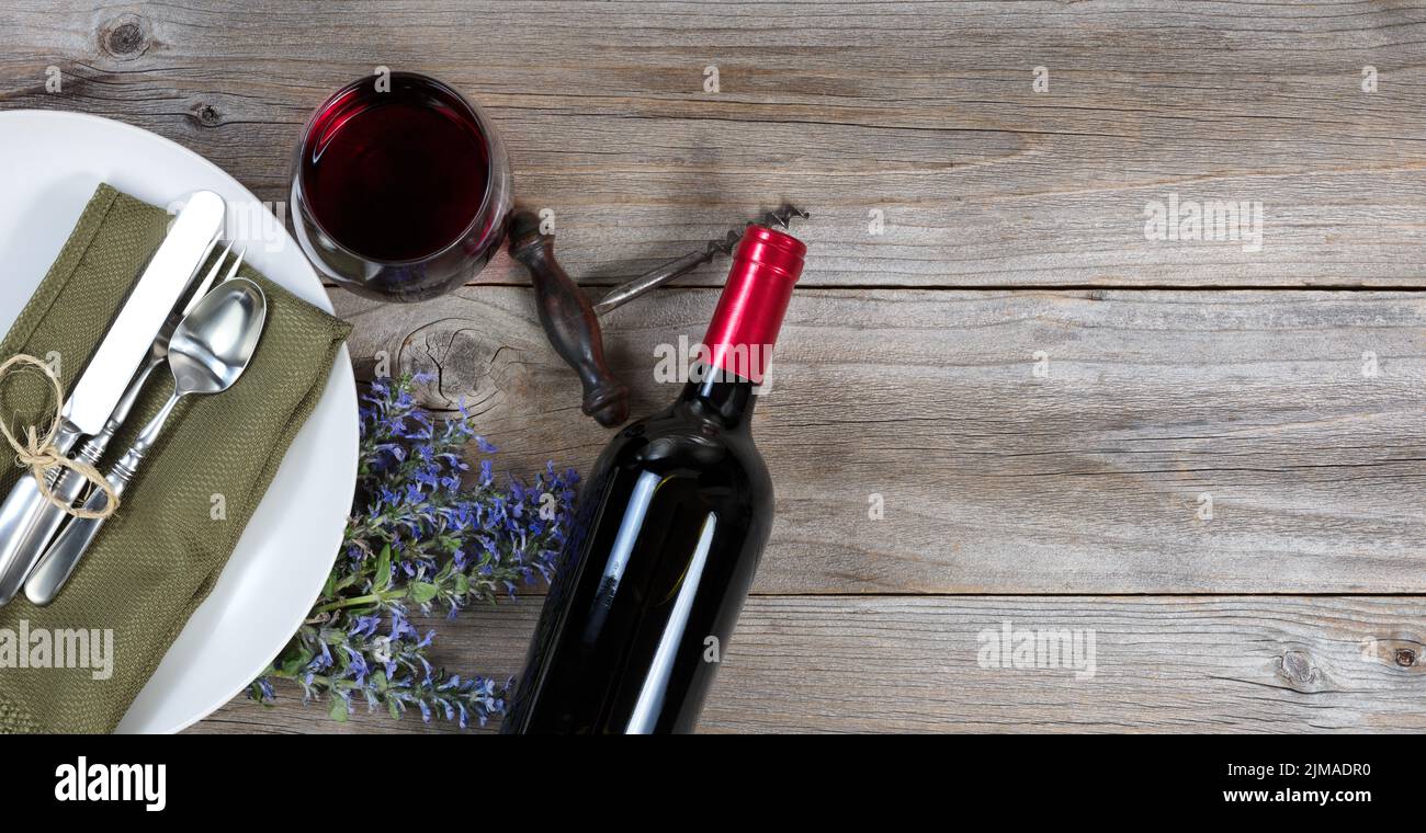 Stoviglie d'epoca su un rustico tavolo in legno con fiori e vino rosso Foto Stock