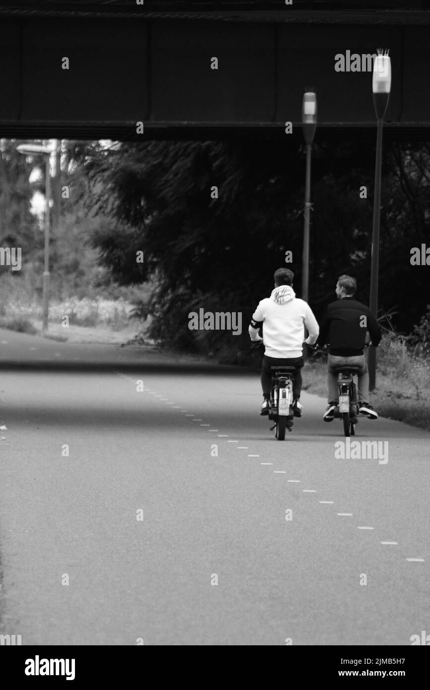 Una scala di grigi, ripresa posteriore di due giovani su ciclomotori nei Paesi Bassi Foto Stock