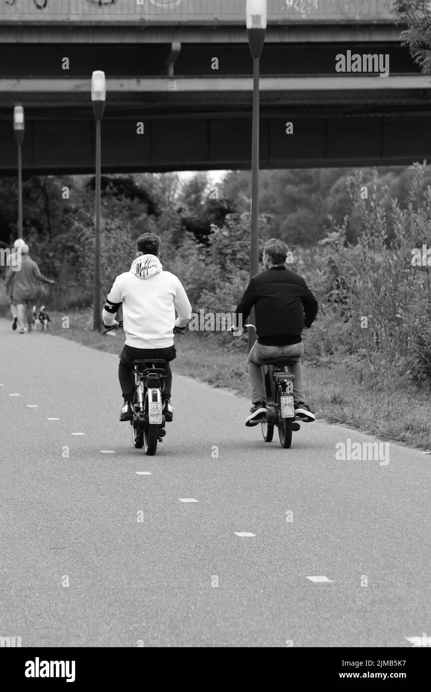 Una scala di grigi, ripresa posteriore di due giovani su ciclomotori nei Paesi Bassi Foto Stock