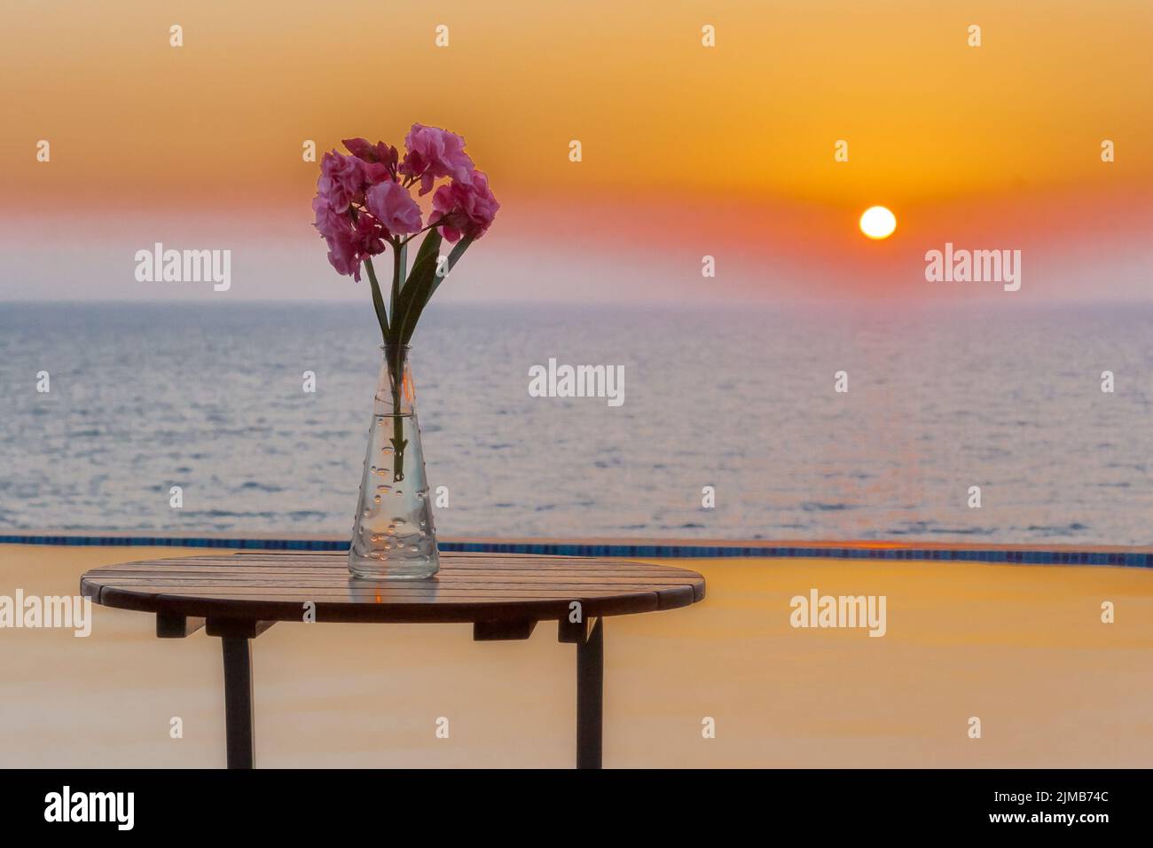 Vaso di fiori sul tavolo a bordo piscina con vista sul mare al tramonto Foto Stock