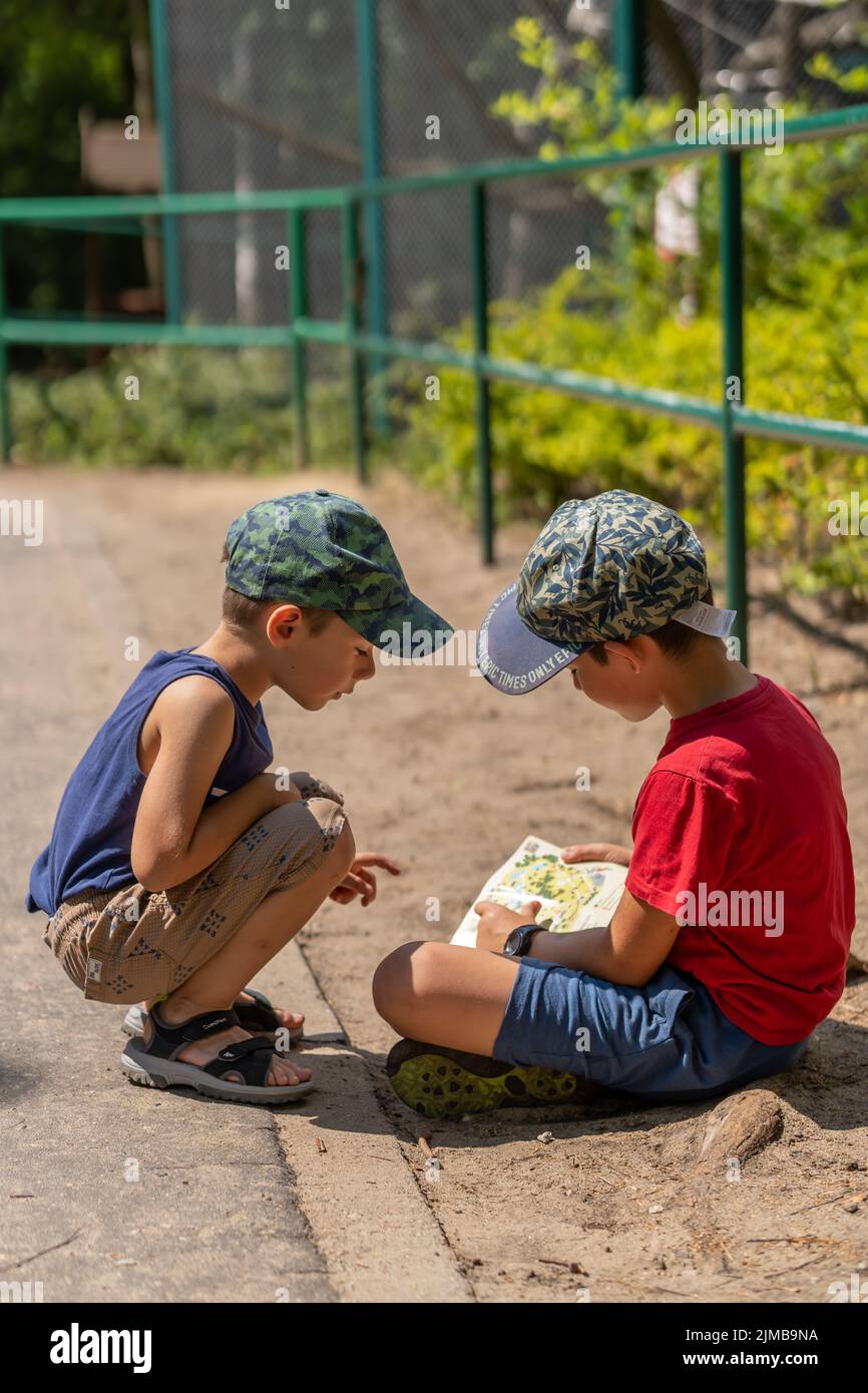 Due ragazzi che si inginocchiano e guardano una mappa con informazioni nel nuovo zoo in una giornata di sole estate. Foto Stock