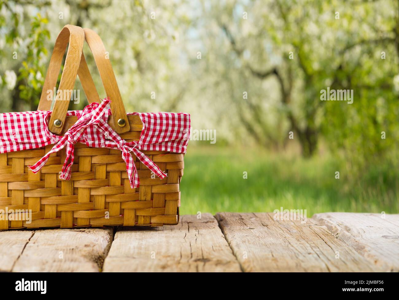 Su un semplice tavolo in legno, un cestino picnic in vimini sullo sfondo di una lussuosa natura estiva. Attività ricreative all'aperto, tradizioni familiari, romanticismo, de Foto Stock