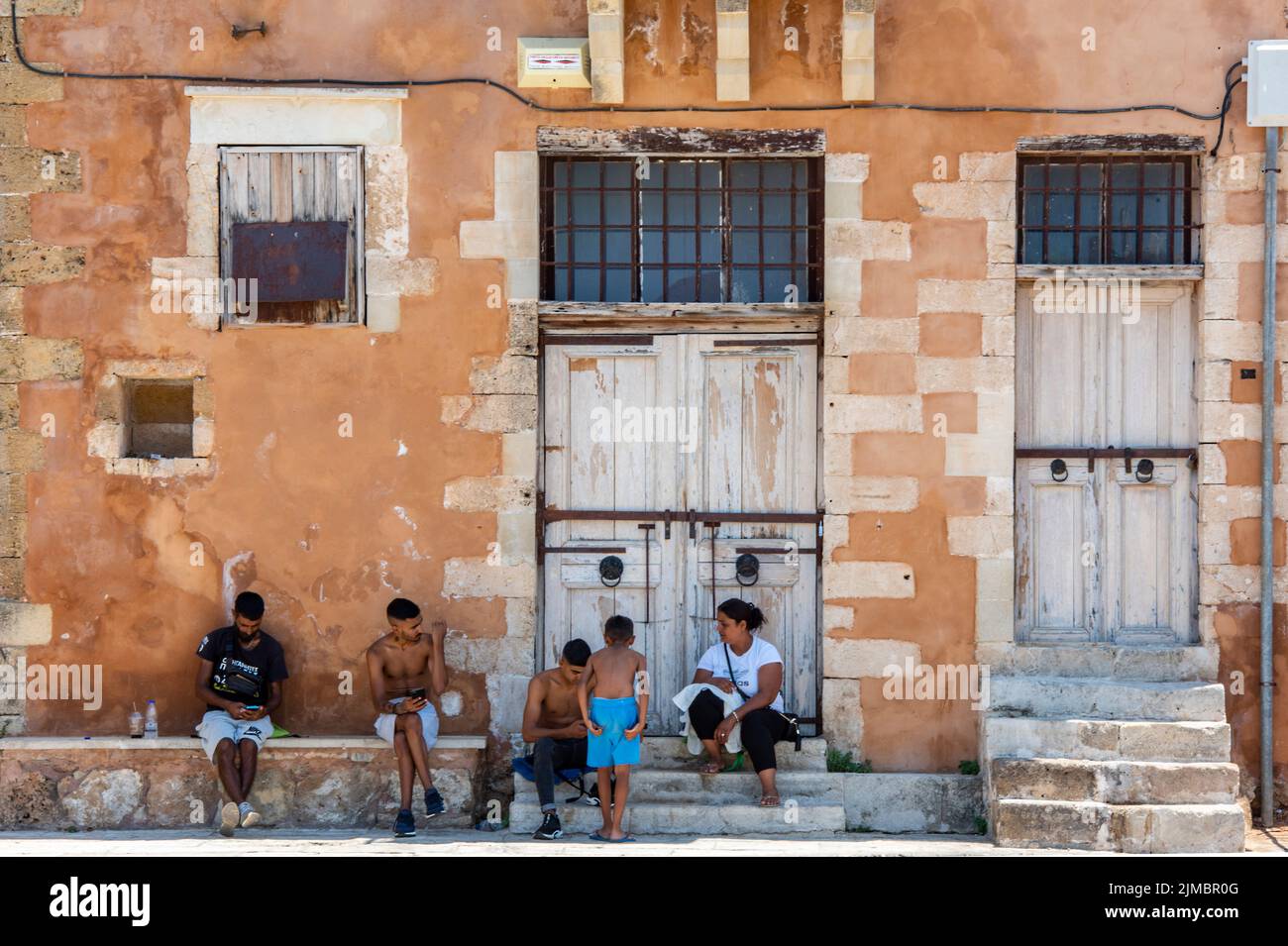 famiglie locali che ombreggiano dal sole di mezzogiorno accanto a un vecchio edificio greco tradizionale sull'isola di creta, nella città di chania. Foto Stock