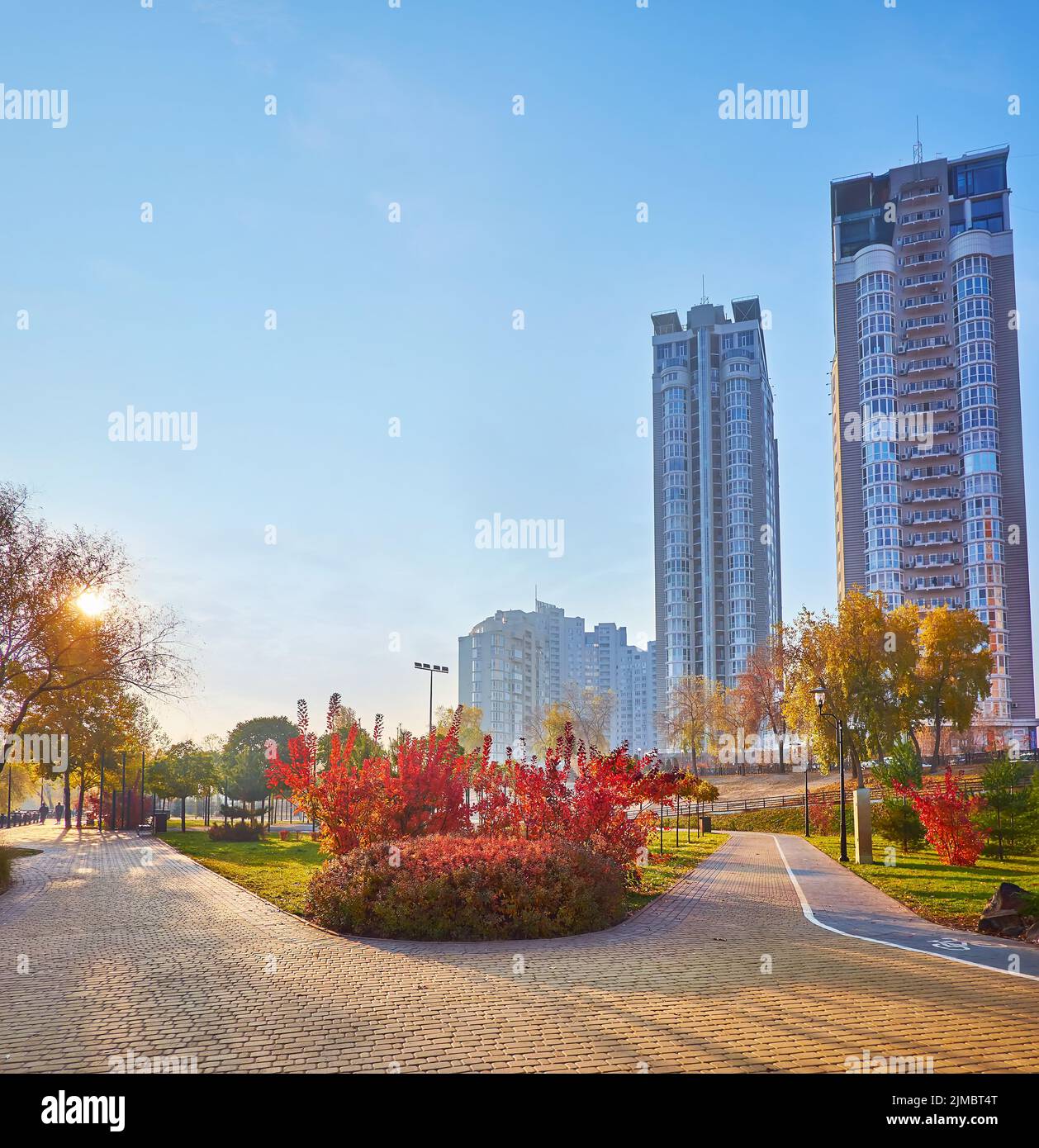 L'alba luminosa nel colorato autunno Natalka Park con viuzze, alberi sparsi e alti edifici residenziali, Obolon, Kiev, Ucraina Foto Stock