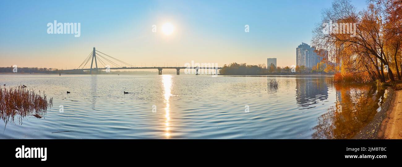 Vista panoramica della riva del fiume Dnieper con alberi d'autunno e il Ponte Pivnichnyi all'orizzonte, Kiev, Ucraina Foto Stock