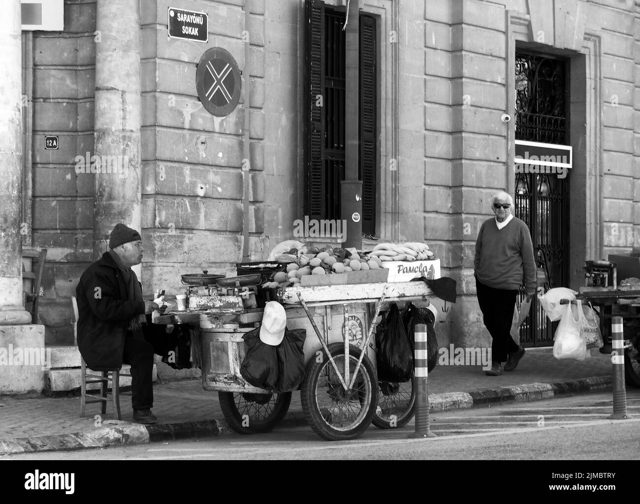 Un uomo che vende frutta da una stalla su un carrello si siede sul marciapiede a Nicosia Cipro su un angolo della strada Foto Stock
