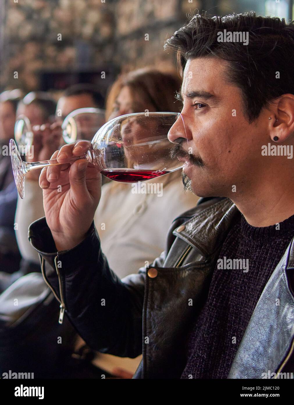 uomo latino di profilo in una degustazione di vini in una cantina a mendoza argentina. Altre persone offuscate sullo sfondo. Uomo brunette in giacca di pelle con un Foto Stock
