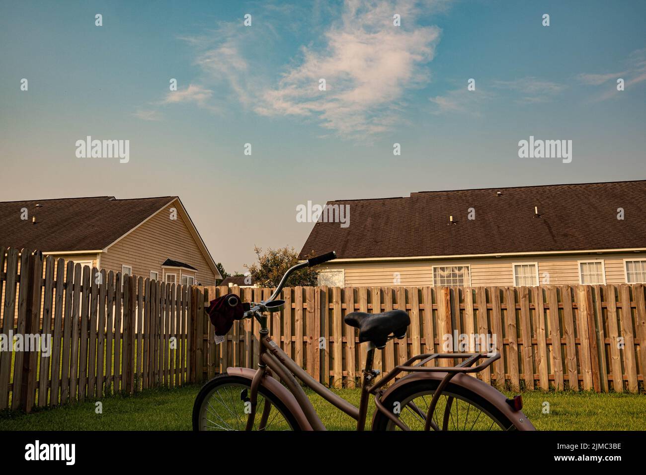 Una bicicletta parcheggiata su un prato casa accanto alla recinzione di legno con altre case visibili dietro la recinzione Foto Stock