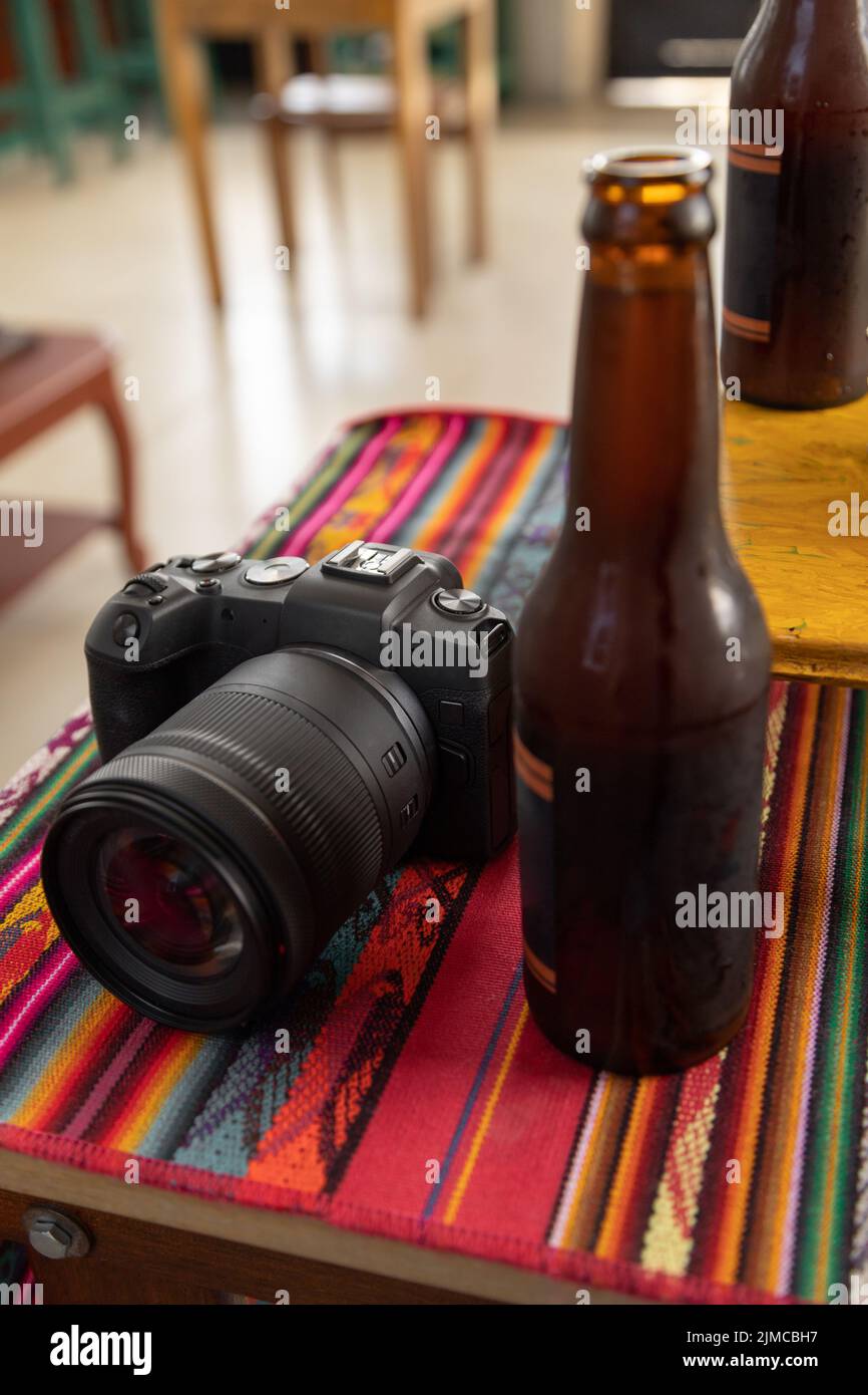 tavolo con tovaglia colorata con fotocamera digitale professionale accanto a una bottiglia di birra, bevanda rinfrescante e tecnologia, strumento hobby, stile di vita Foto Stock