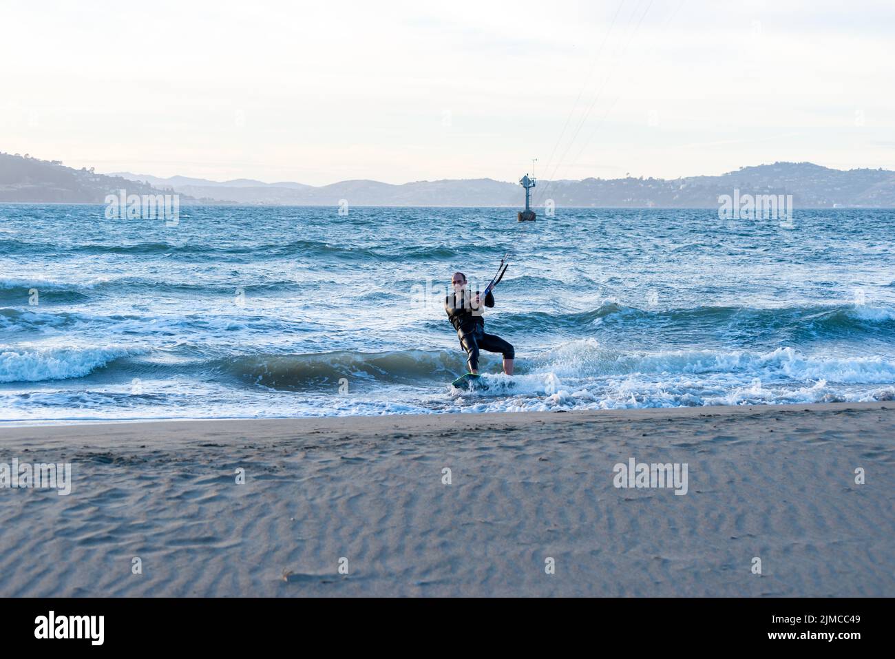 Kitesurfer maschio vicino al bordo di un corpo d'acqua con acqua blu e colline in lontananza Foto Stock