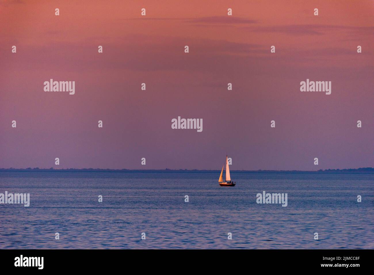 Una barca a vela Singe galleggia su Mobile Bay al tramonto. Foto Stock