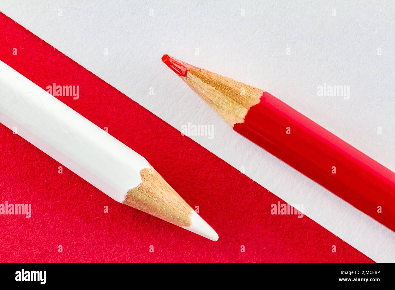 Matite colorate su carta rossa e bianca disposte diagonalmente. Foto Stock
