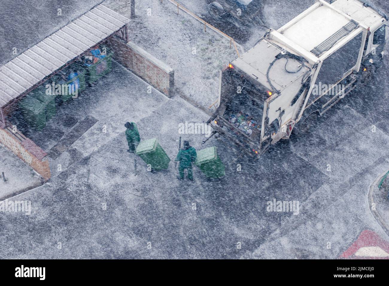 Veicolo per la raccolta rifiuti e due lavoratori nella tempesta di neve, vista dall'alto Foto Stock