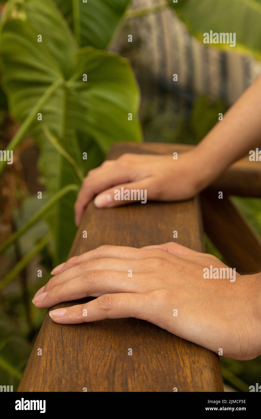 mani di una persona che si avvicina a un corrimano in legno sullo sfondo foglie naturali di un giardino, dettagli texture, carta da parati natura con parte del corpo Foto Stock