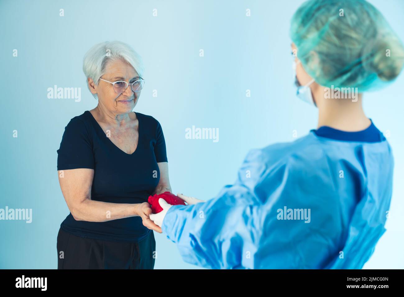 Una donna felice anziana europea e un medico chirurgo in un abbigliamento medico protettivo che tiene rosso cuore artificiale . Foto di alta qualità Foto Stock