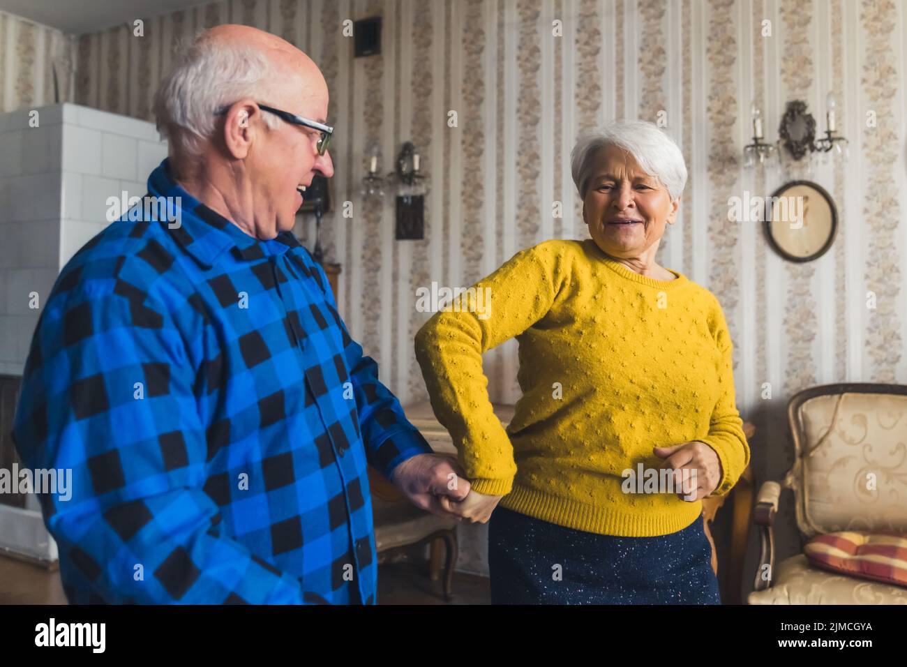 Gioiosa anziana caucasica che balla insieme con il marito felice nel soggiorno della propria casa. Foto di alta qualità Foto Stock