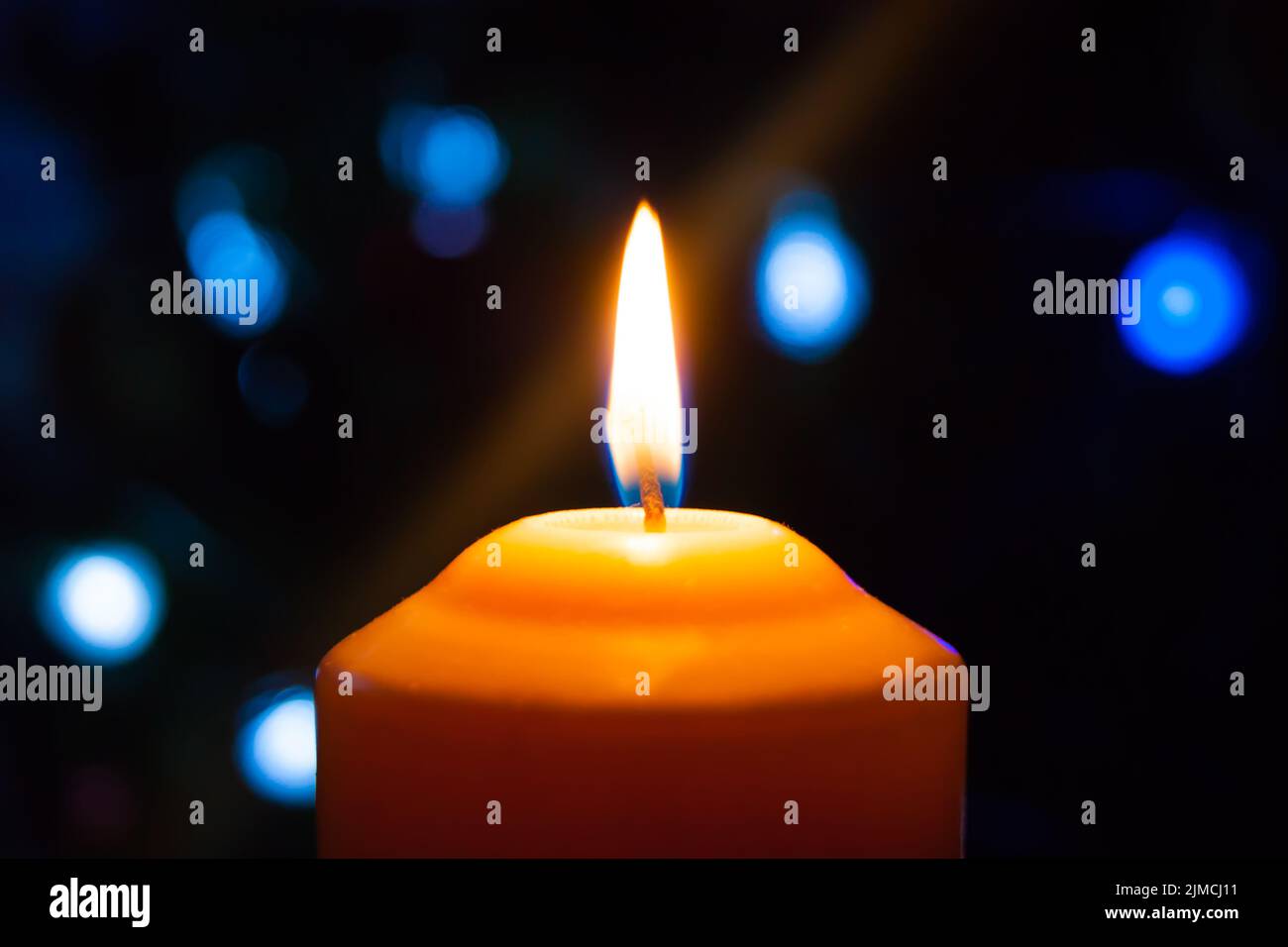 Una candela arancione che brucia su uno sfondo scuro con luci blu - una vigilia di Capodanno di Natale divination mystic esoteric romance lo Foto Stock