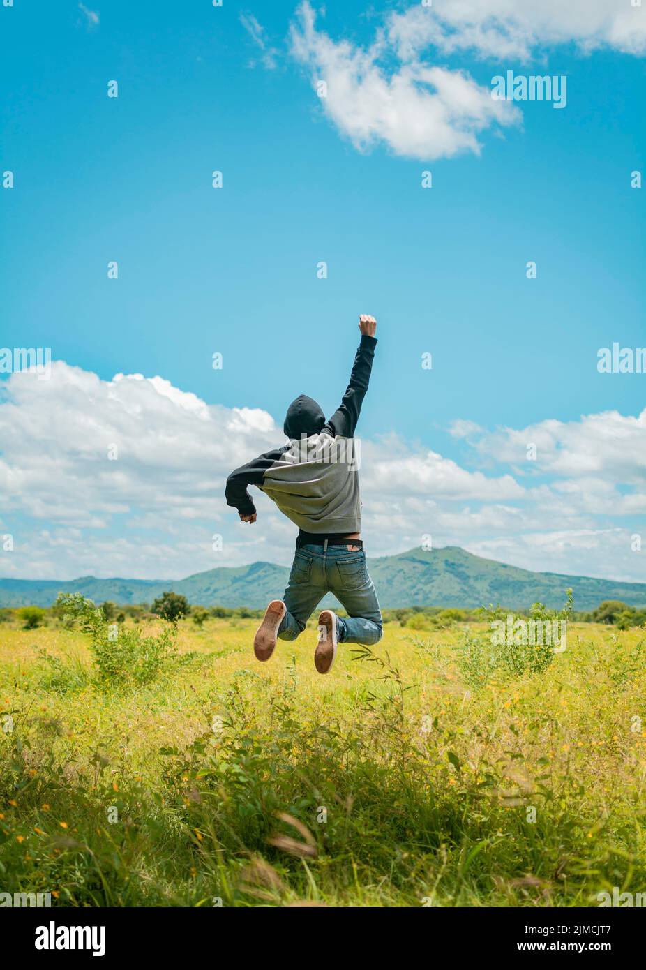 Vista posteriore dell'uomo che salta nel pugno di raccolta erba, concetto di una persona libera che salta e alza il braccio, persona libera che salta con felicità nel Foto Stock